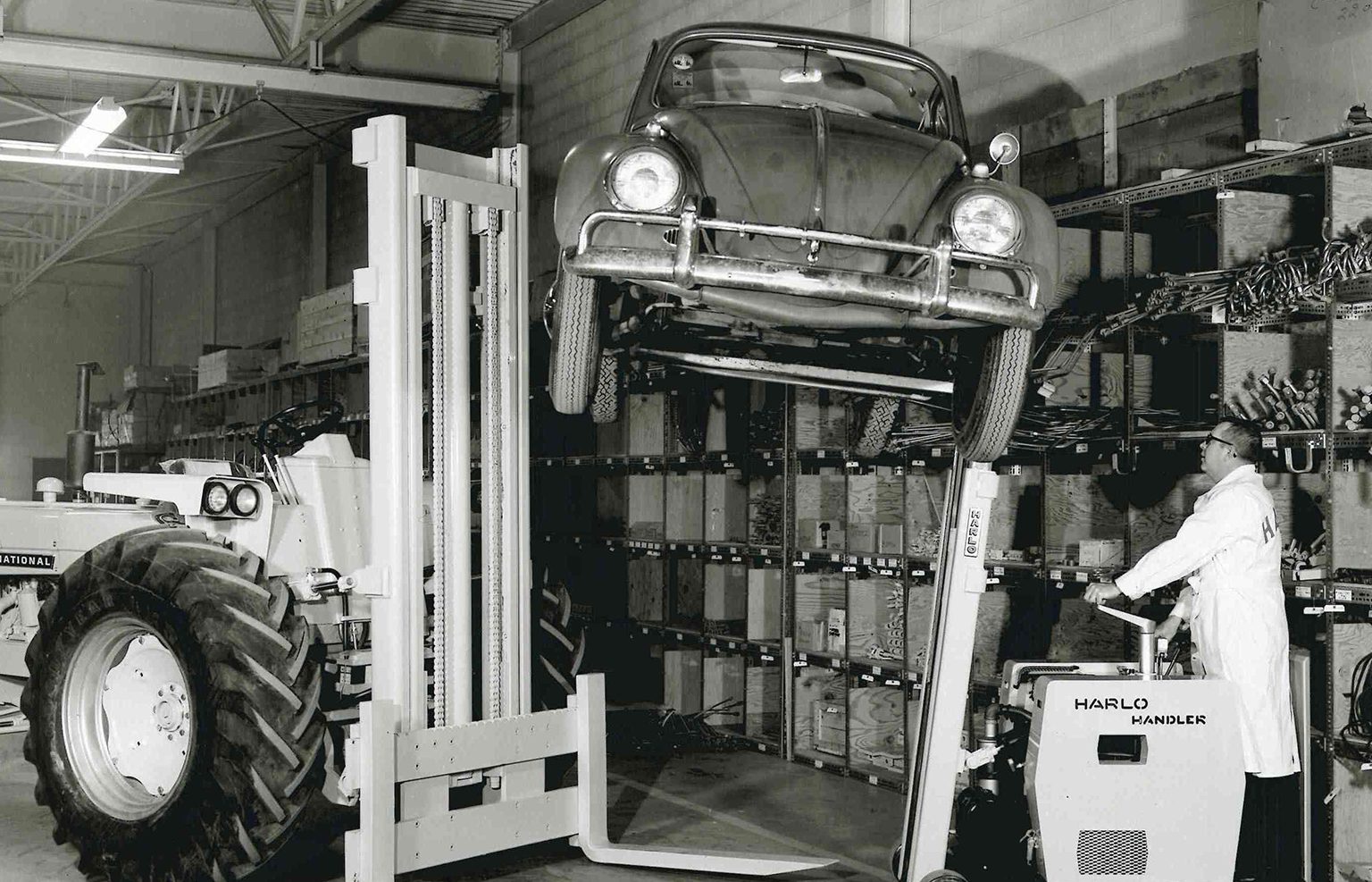 Historic photo of a vintage Harlo Handler lift raising an automobile in a warehouse