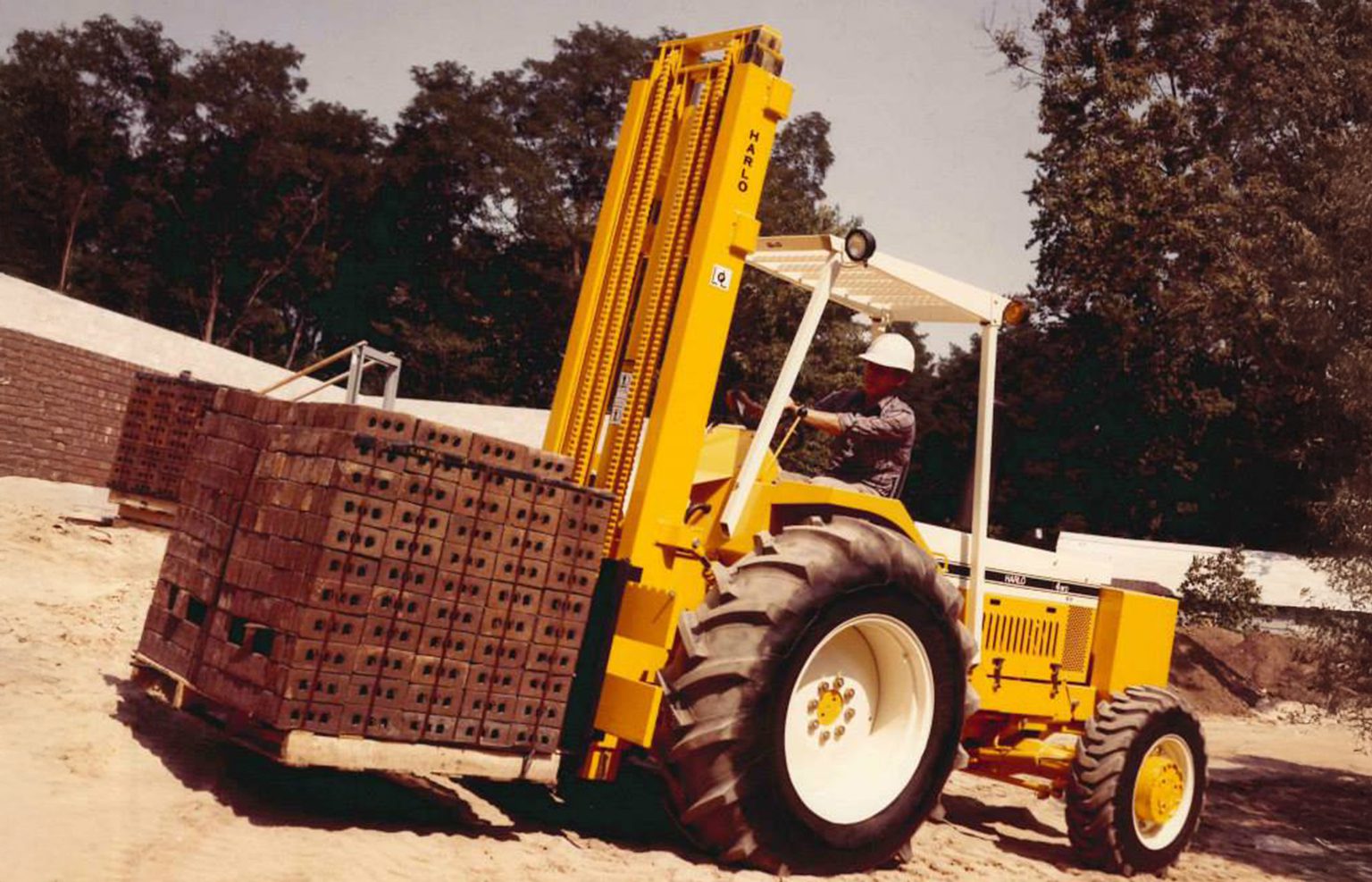 Vintage photo of a Harlo rough terrain forklift carrying a load of bricks on a job site